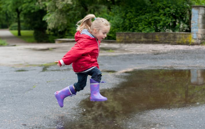 Happy child in rain boots and coat jumping into a puddle and engaging in unstructured play