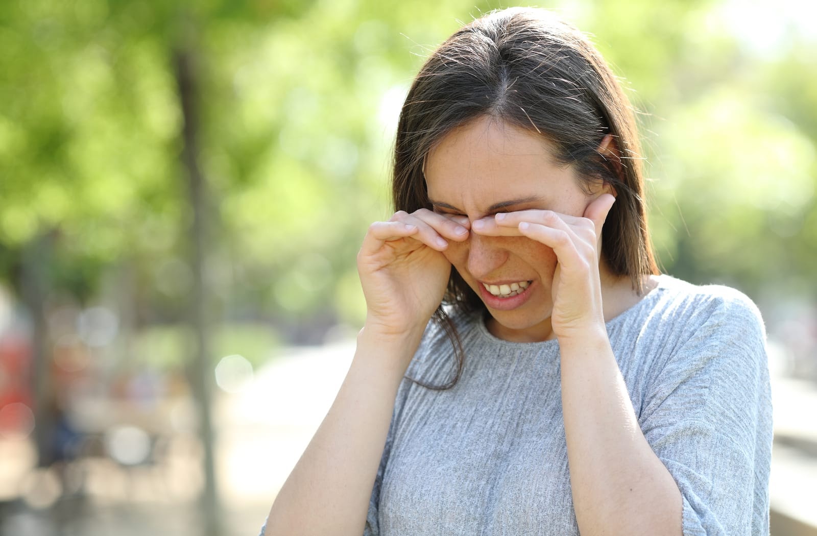 Woman standing outside in a park rubbing her eyes due to dry eye from allergies