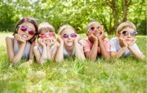 Six kids laying on the grass with sunglasses on to protect their eyes from the sun