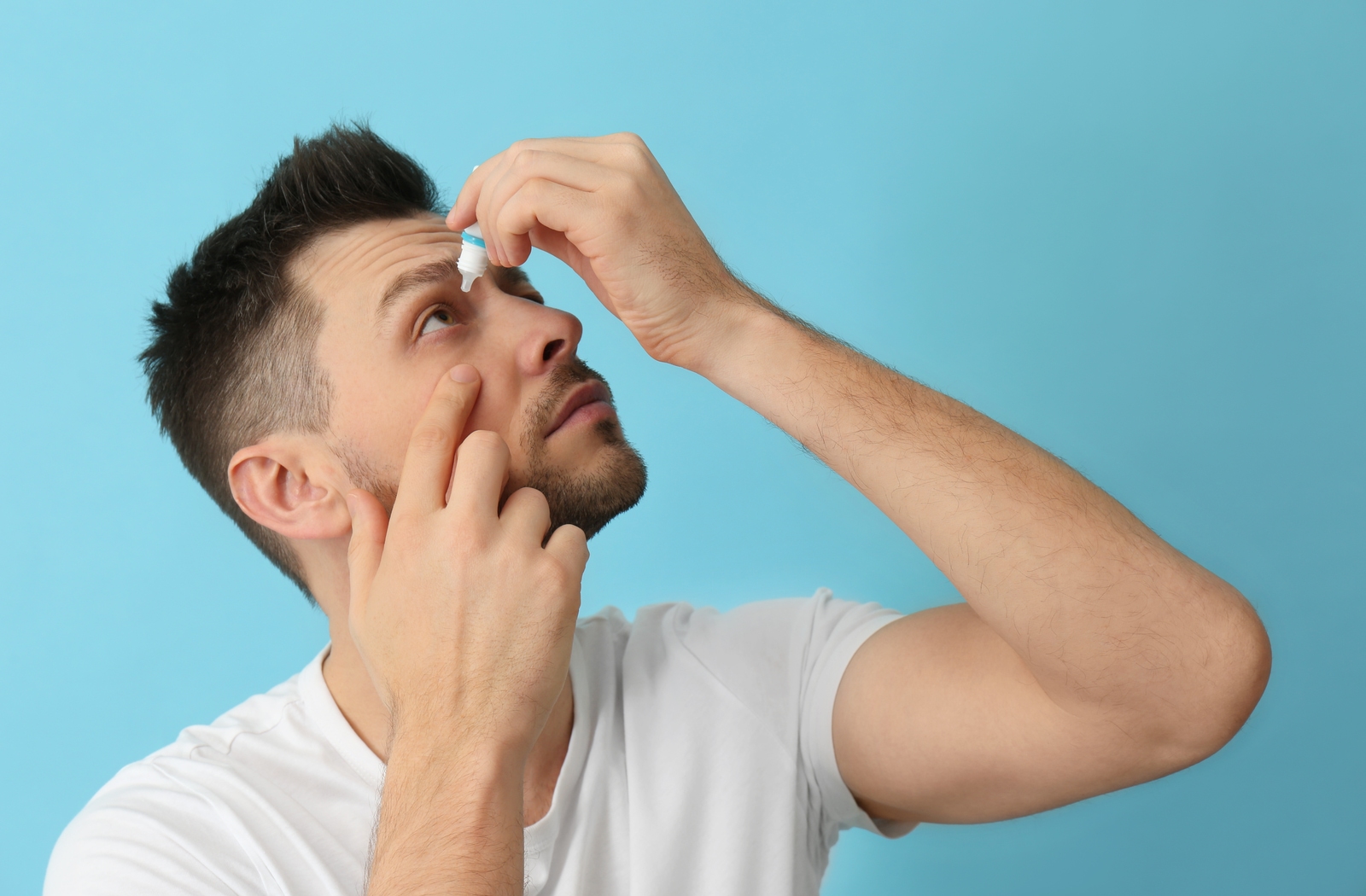 Man in front of a blue background putting in eye drops to try and relieve his dry eye