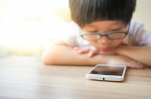 A young boy with glasses looking closely at a smartphone screen putting him at risk for digital eye strain