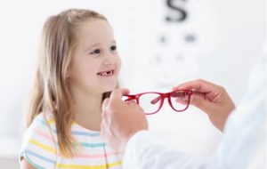 A young girl that just finished getting her regular eye exam at her optometrist picking out new, red glasses