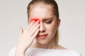 A woman touching her left eye in discomfort as it is highlighted in red to symbolize the feeling of pain and irritation