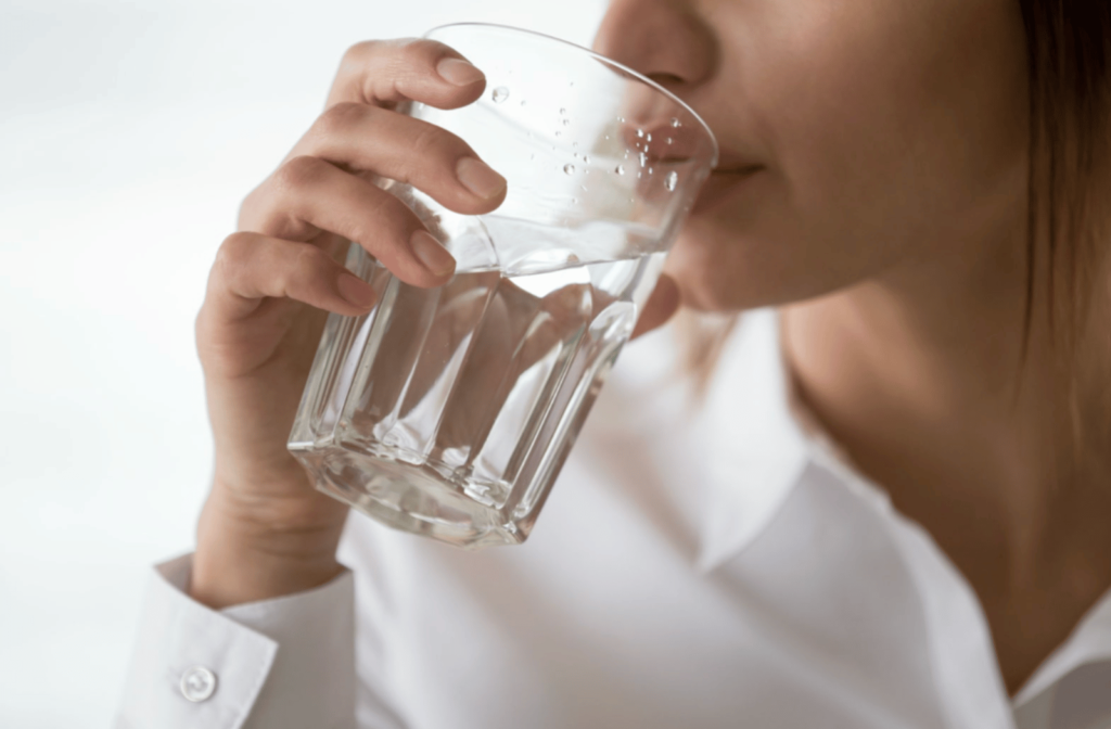 A woman drinking a glass of water to keep herself from dehydrating
