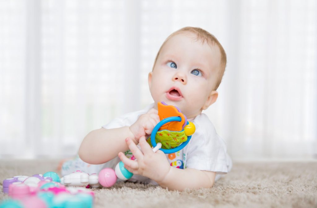 A baby with crossed eyes present is playing with a few different rattles and toys made for babies