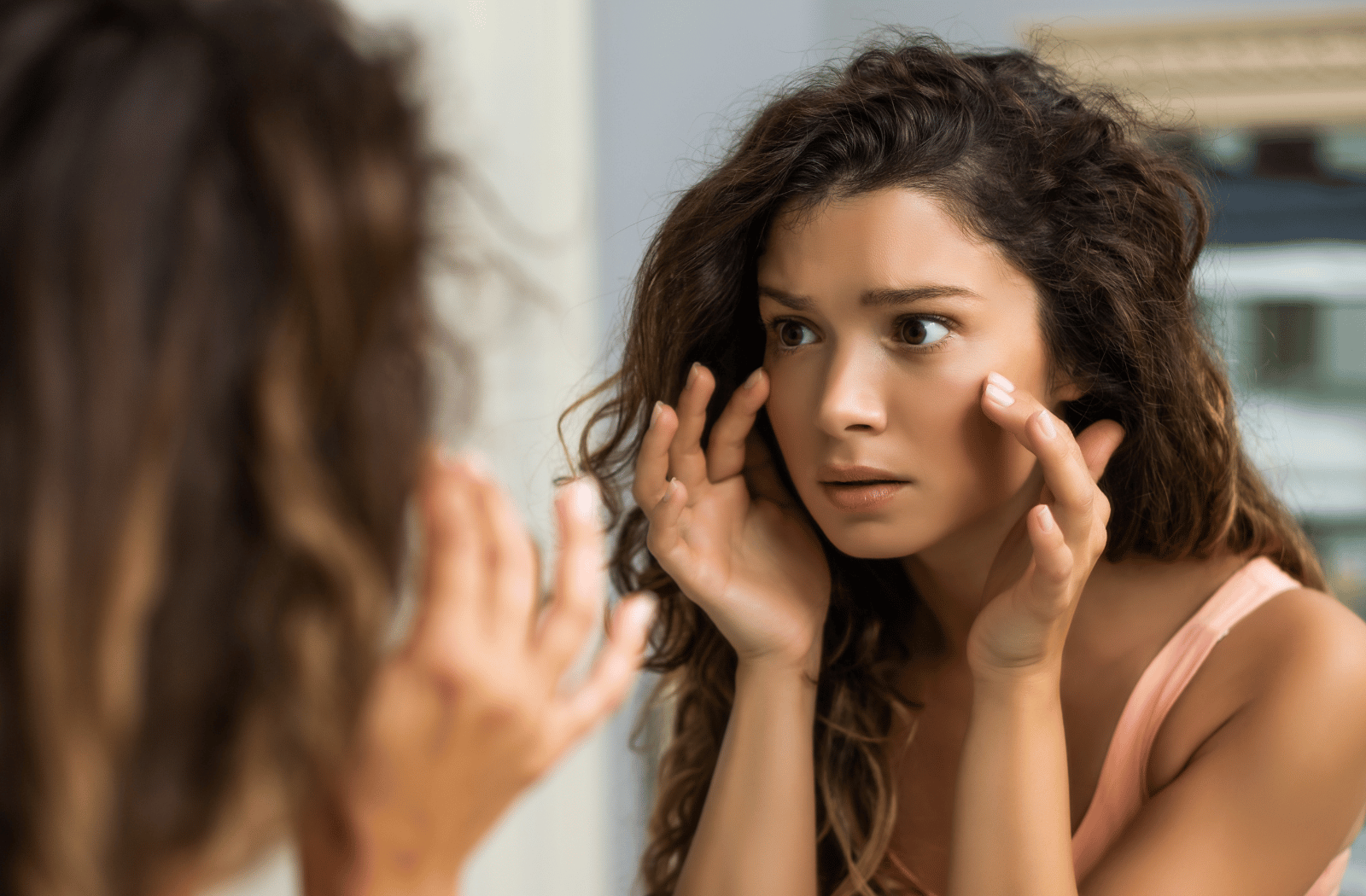 A young woman examines her eyes in the mirror due to eye twitching that won't stop.