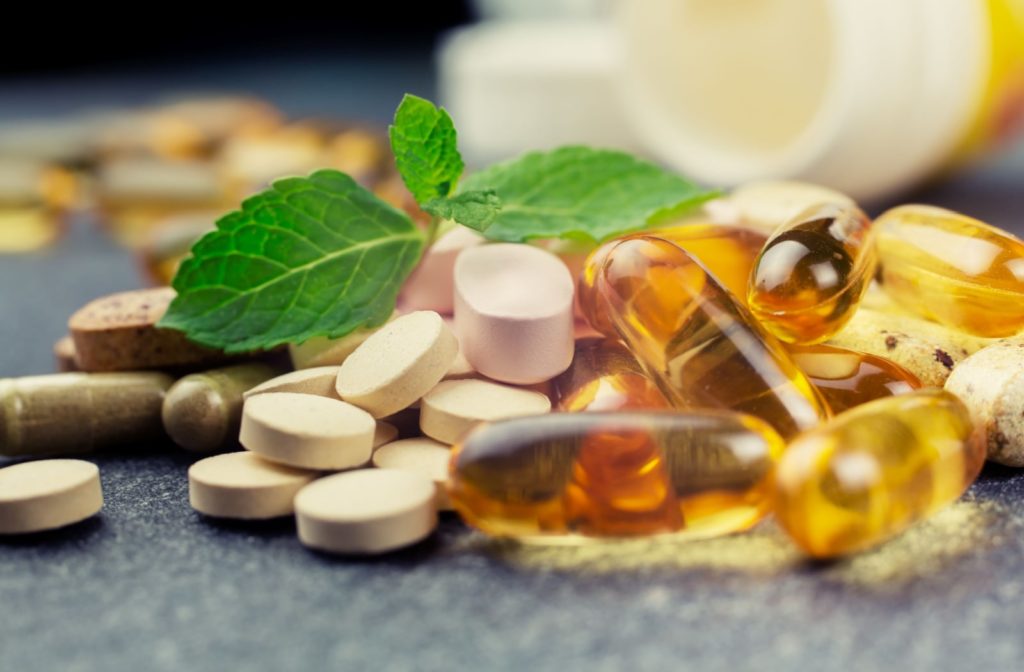 A close-up of an assortment of multivitamin capsules and tablets. Atop of them is a mint leaf.