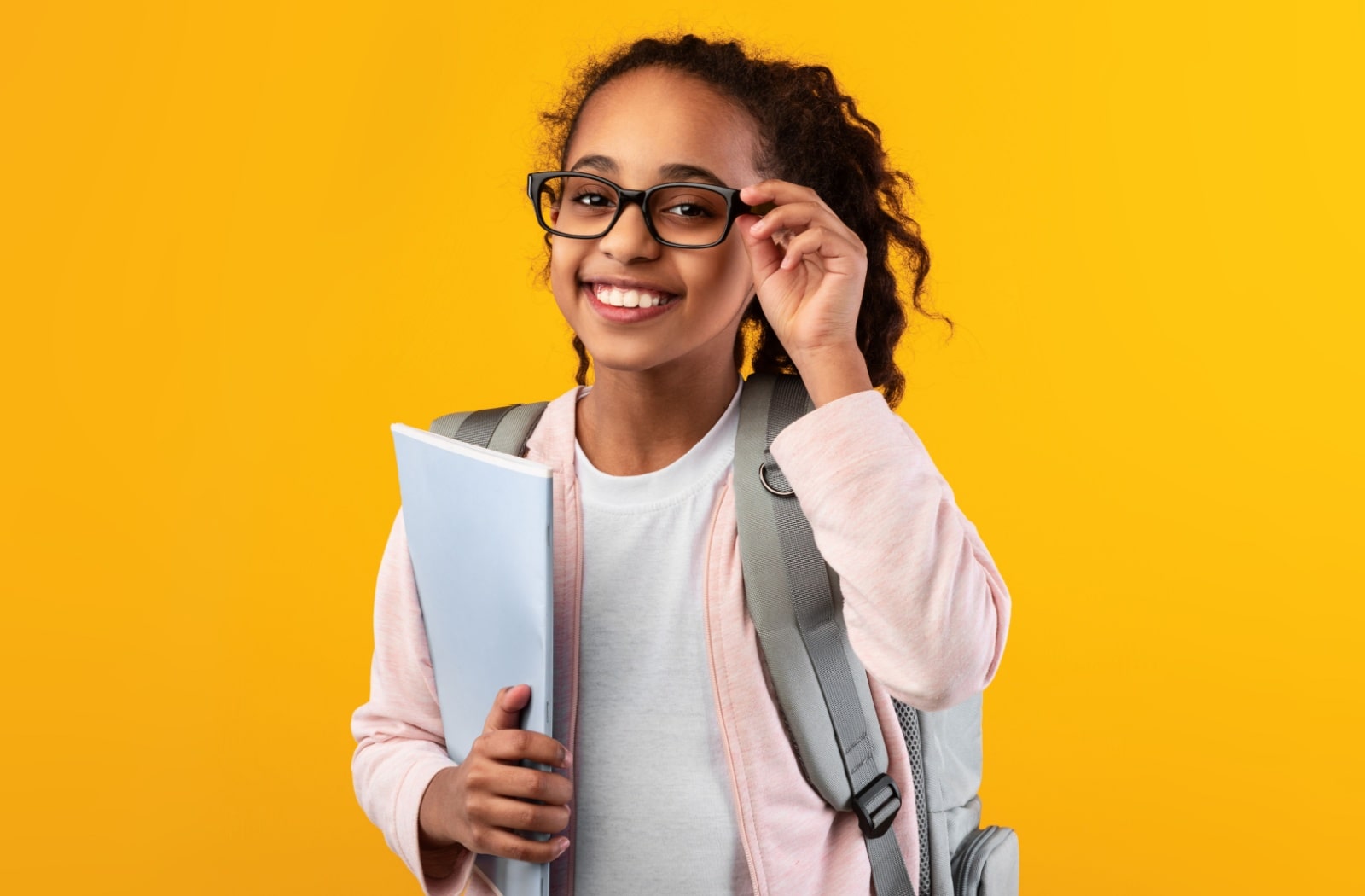 A young girl wearing a backpack and holding onto a folder. She's wearing glasses as a myopia management method.