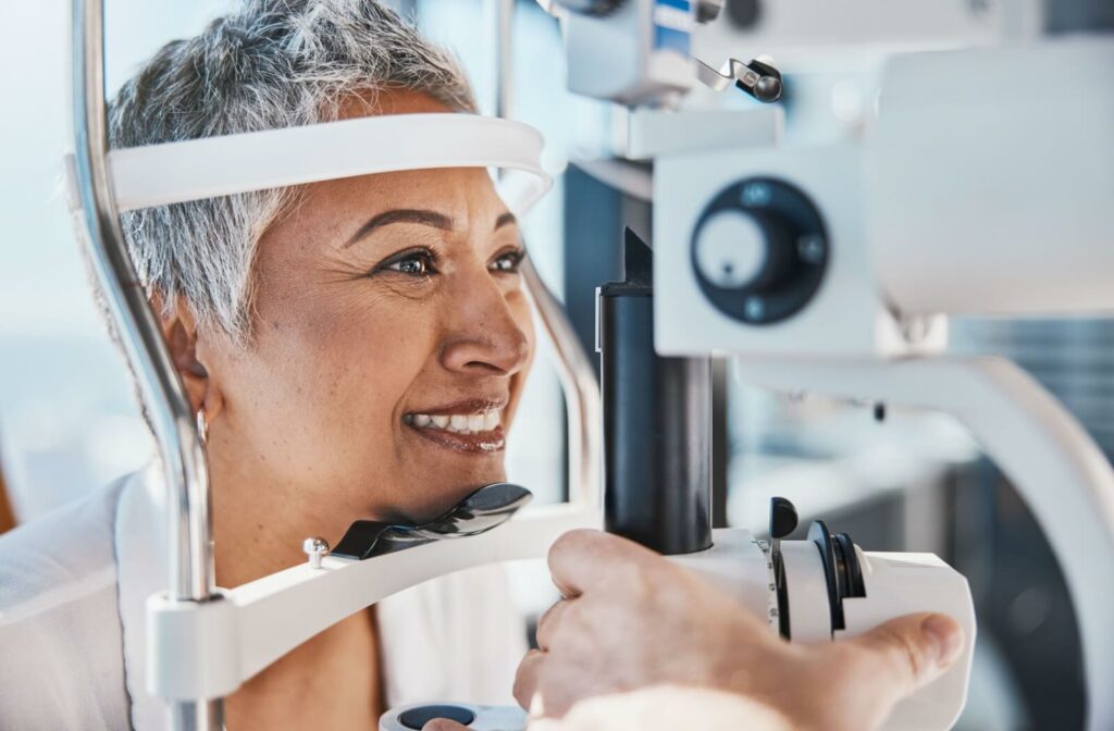 A senior woman smiling while an out-of-frame optometrist carefully checks her eyes during an eye exam.