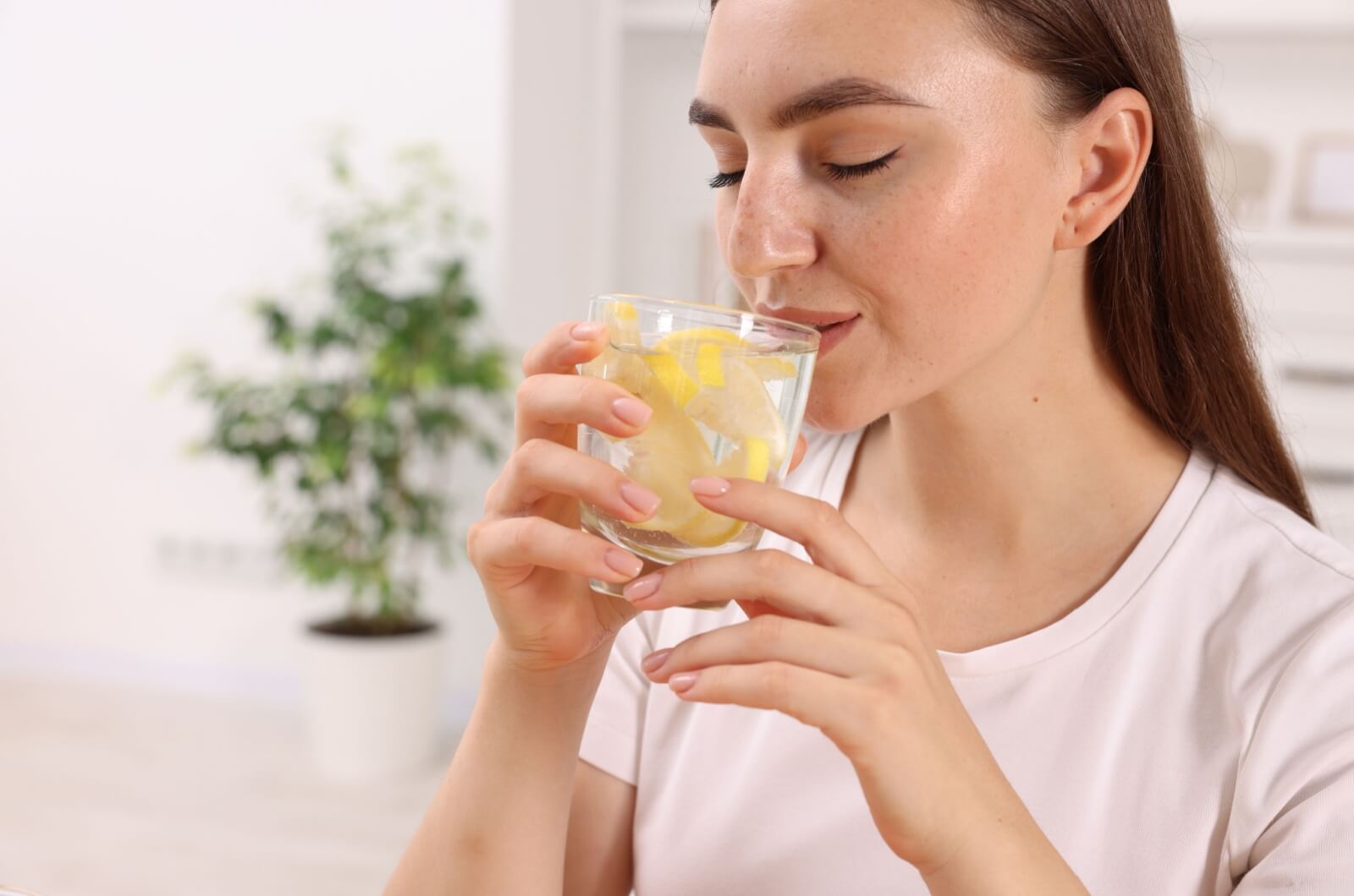 A young adult closes their eyes as they take a sip of a glass of water with lemon slices