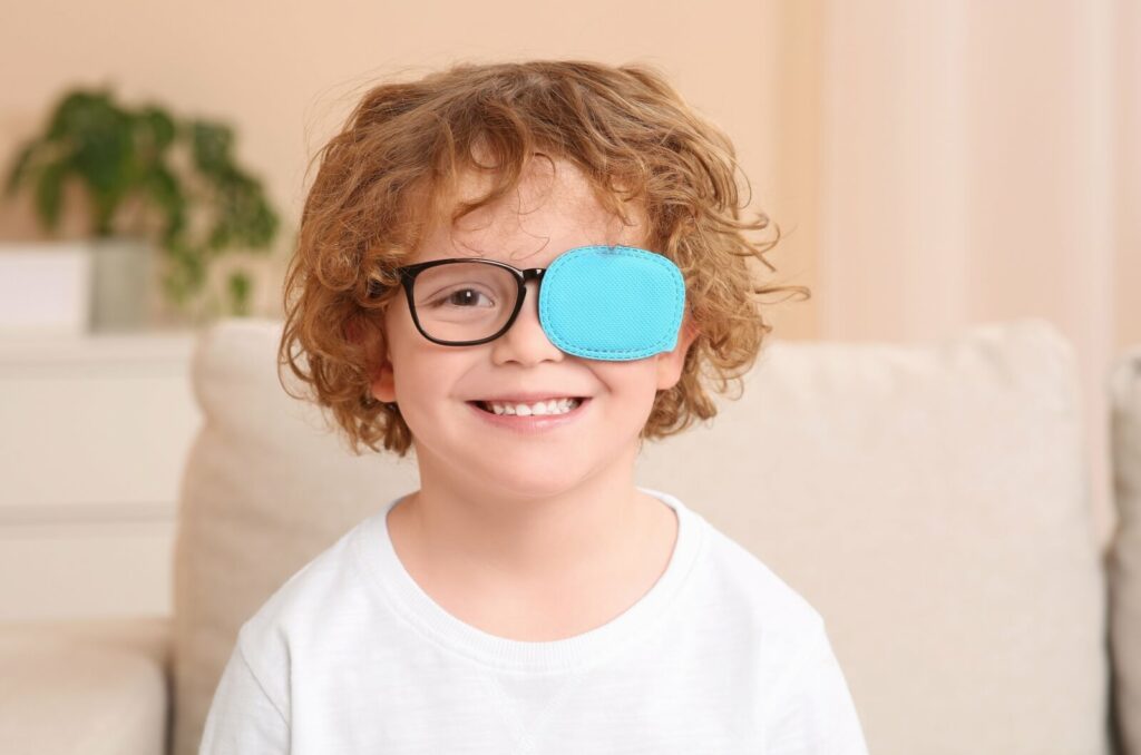 A little boy smiles while wearing an eye patch over his left eye.