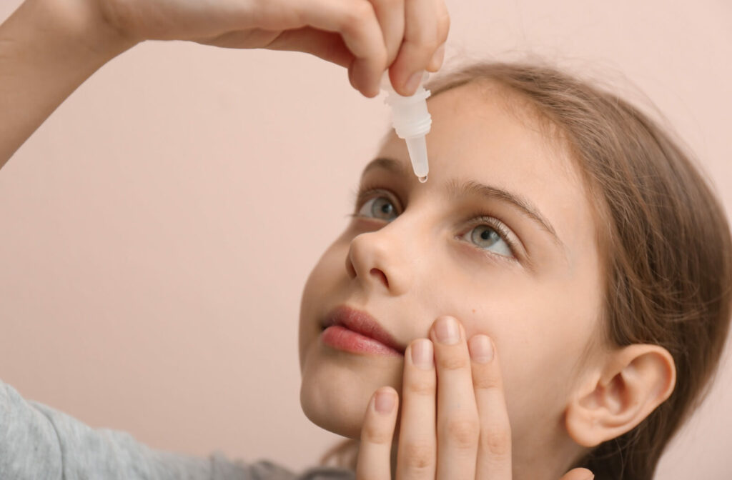 A close-up image of a young child carefully applying eye drops to their left eye.