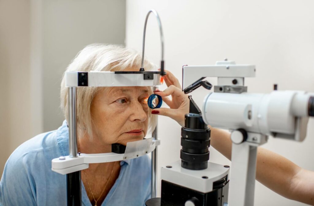 An older adult looking through a lens in front of optical equipment during an eye exam.