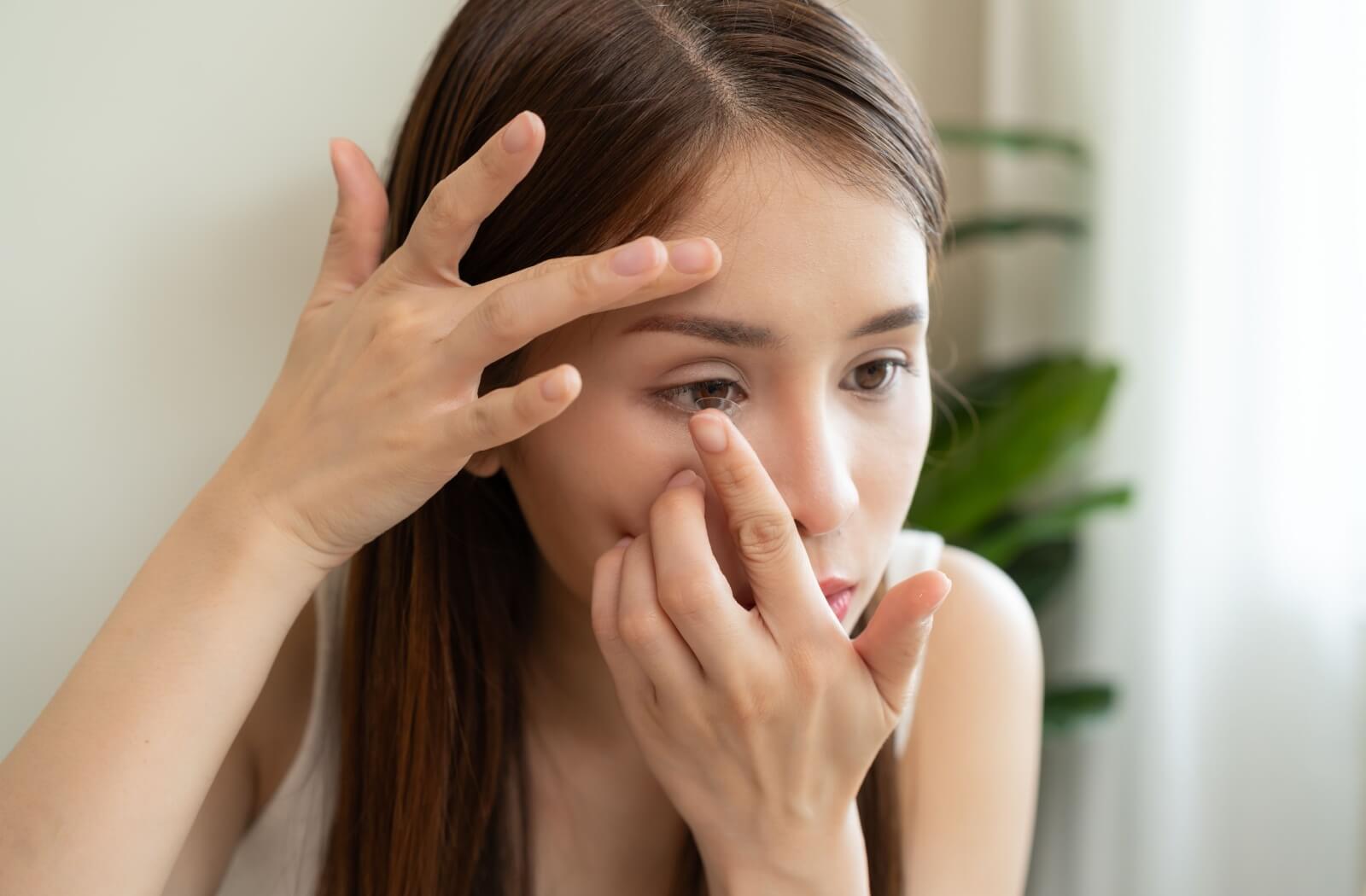 A young adult carefully removing an inside-out contact lens from their right eye.