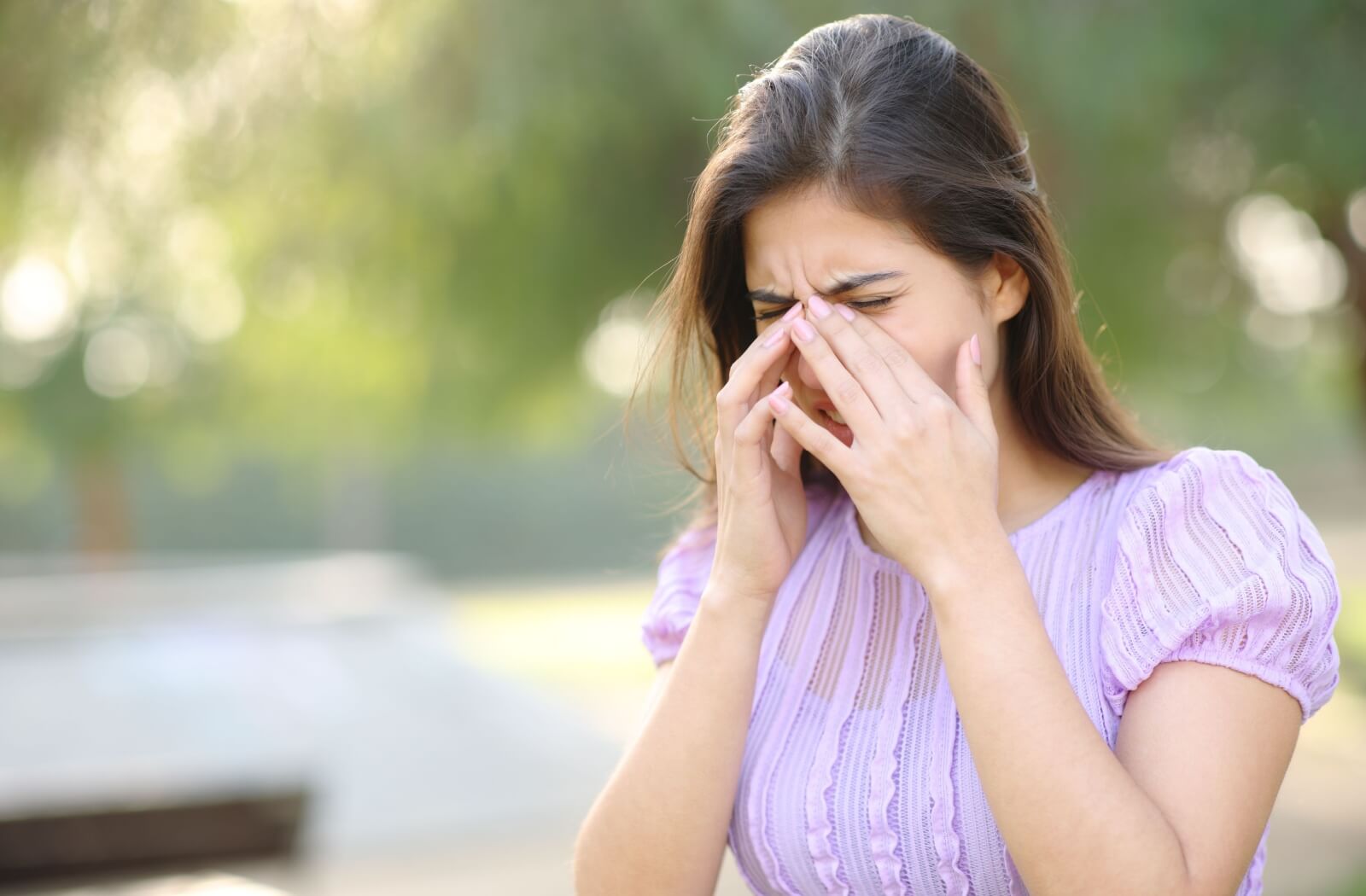 A young adult rubbing their eyes outside due to irritation from the common cold.