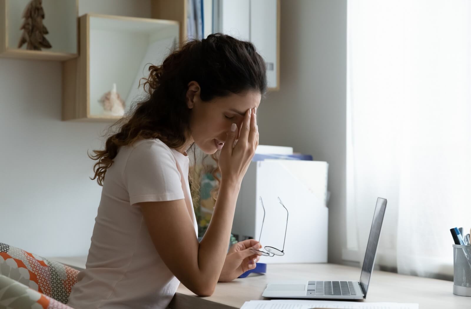 Woman experiencing eye strain and holding her head in discomfort while working on a laptop, possibly due to dry eye symptoms.