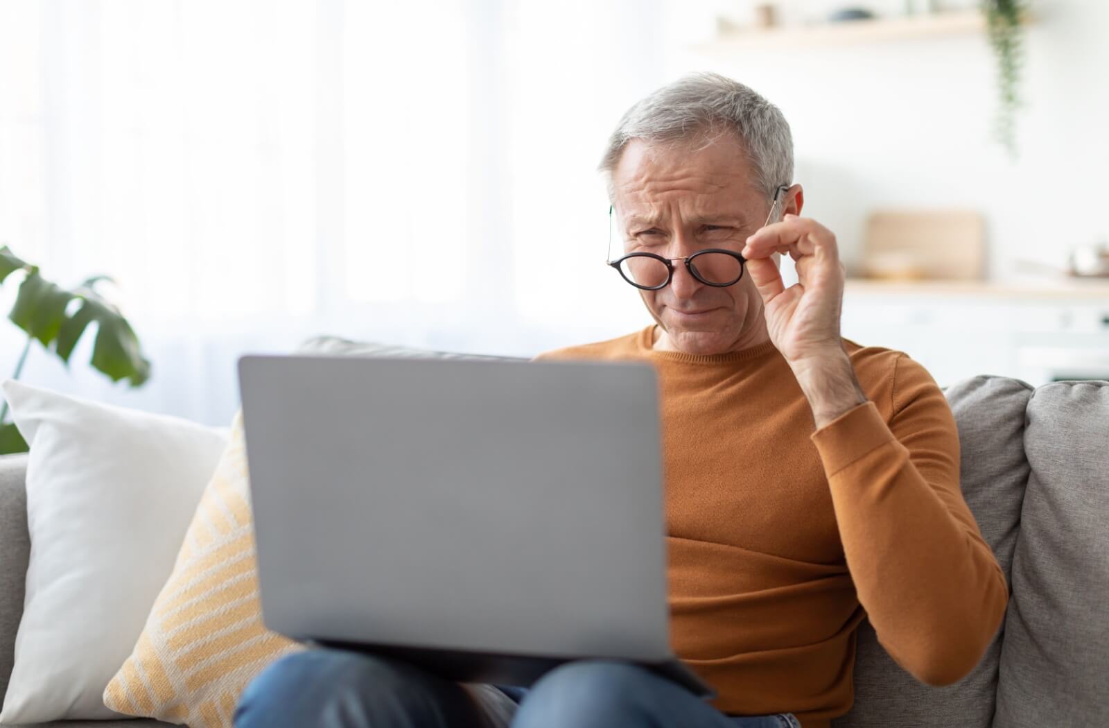 Man squinting at laptop screen while sitting on a couch at home.