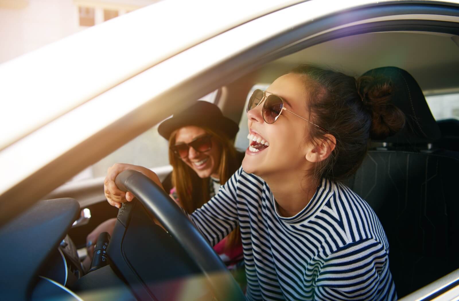 A young adult laughs with a friend while driving. They are wearing polarized lenses to reduce sun glare.