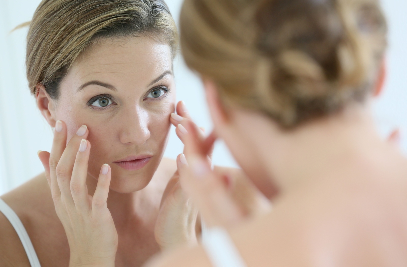 A woman looking in the mirror at her eyes because they are twitching.