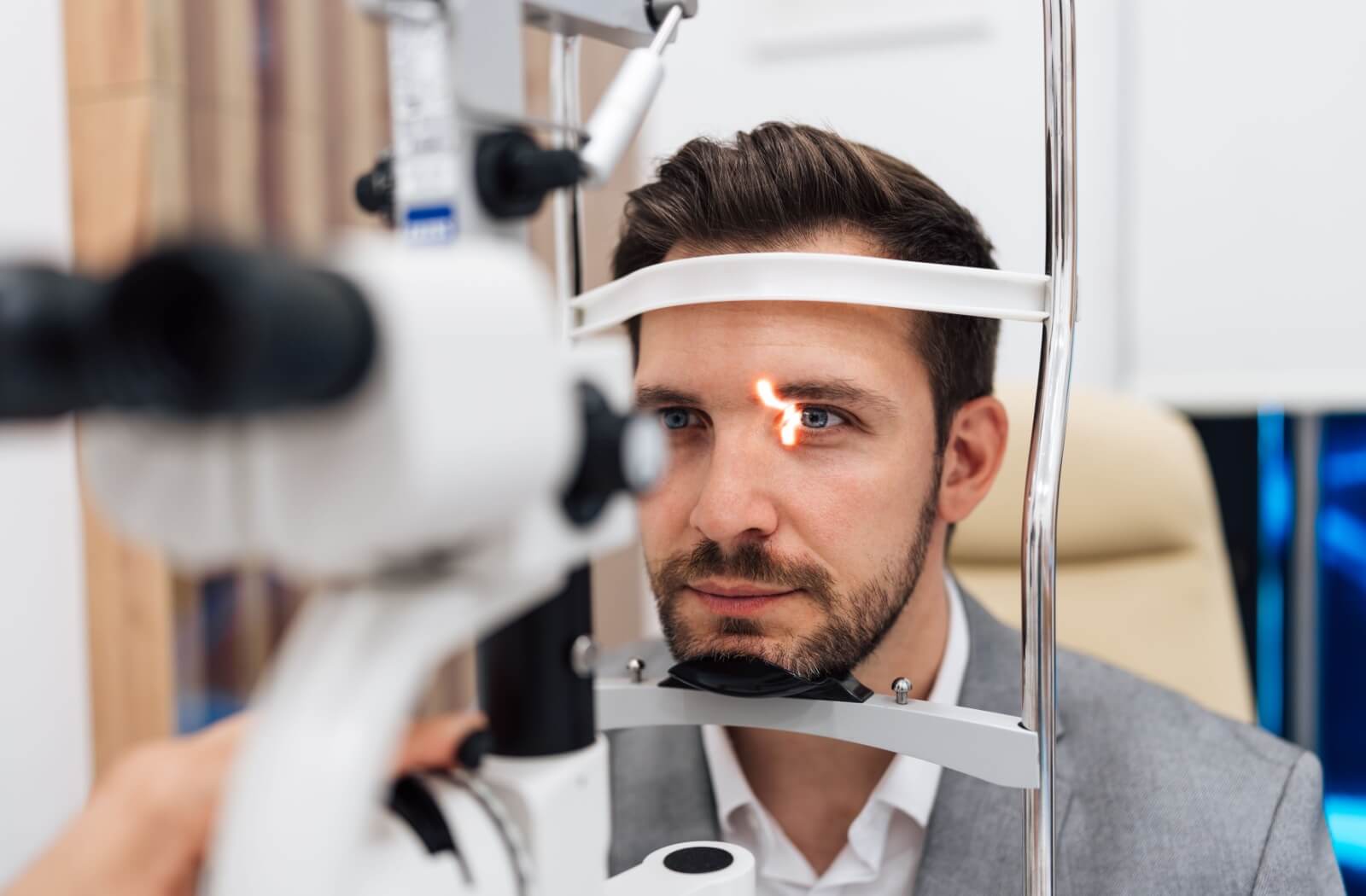 Man undergoing an eye exam with a slit lamp machine at an optometrist’s office.