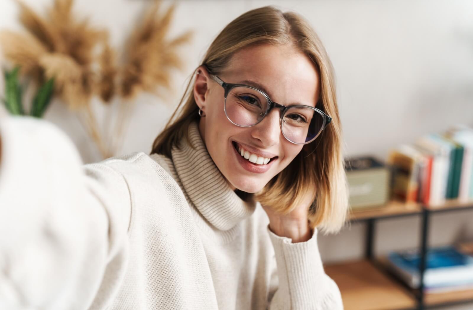 A smiling person wearing glasses and a turtleneck sweater taking a selfie.