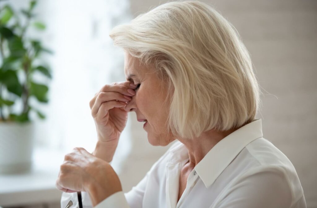 A person rubbing the bridge of the nose in discomfort, illustrating the eye strain and fatigue often associated with managing hereditary vision risks.